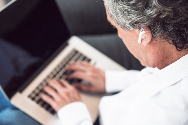 An overhead view of senior man wearing bluetooth earphone using laptop