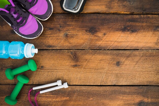 An overhead view of shoes; dumbbells; skipping rope; water bottles on wooden table