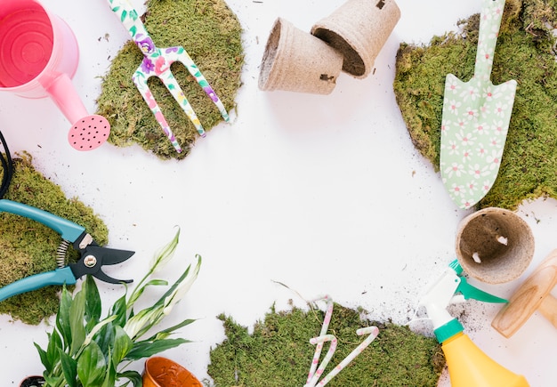 Overhead view shovel; gardening fork; pruner; watering can; turf; spray bottle on white backdrop