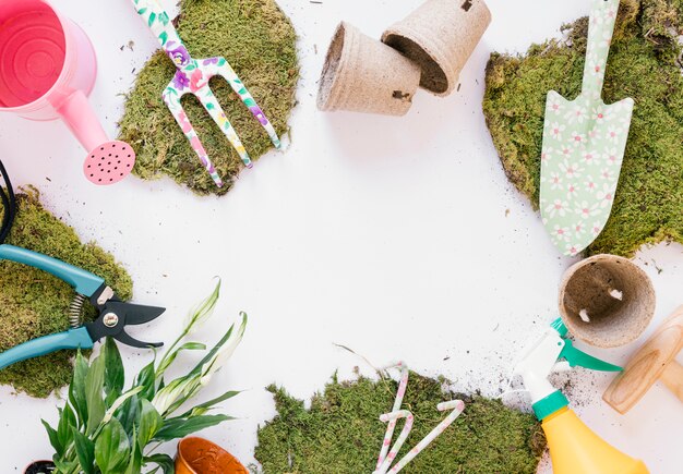 Overhead view shovel; gardening fork; pruner; watering can; turf; spray bottle on white backdrop