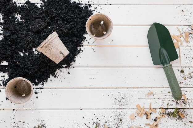 Overhead view of shovel; seedling peat pots; and soil over dirty wooden bench