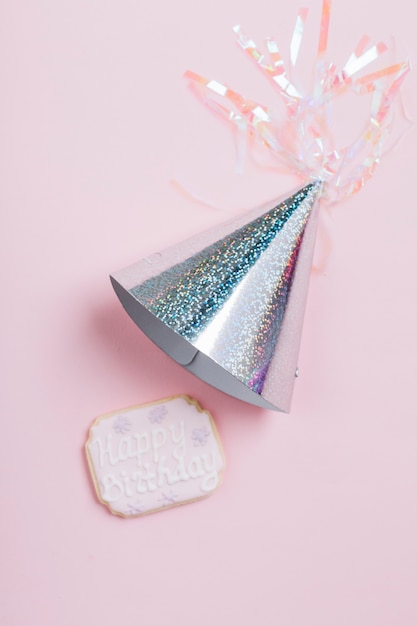 Free photo overhead view of silver birthday hat and cookie on pink background