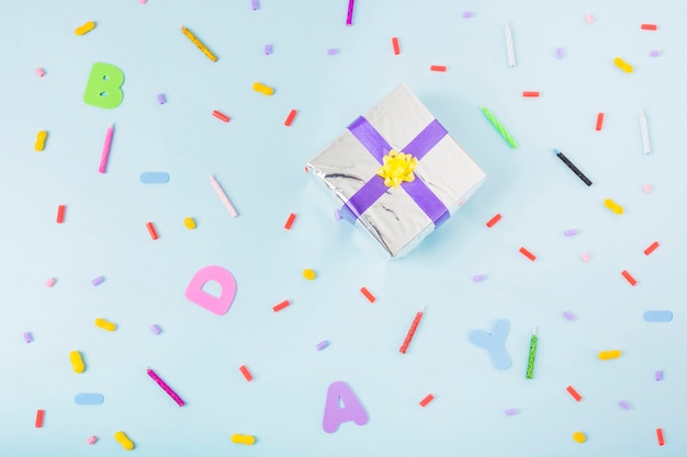 Overhead view of silver gift box surrounded with candies and candles on birthday