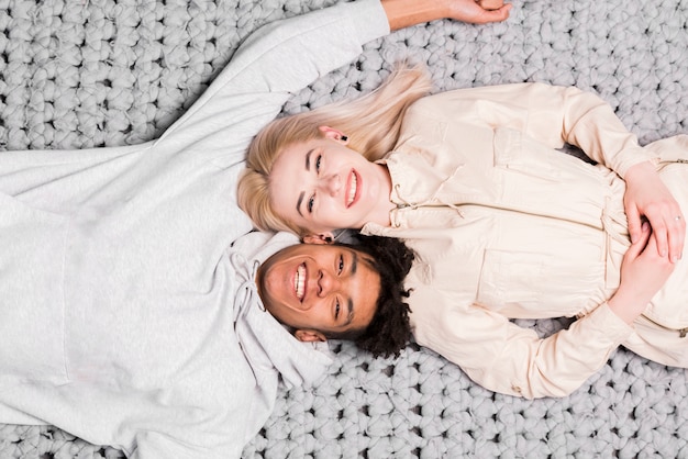 Вид сверху улыбающиеся межрасовые молодая пара, лежа на сером ковре