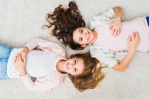 Foto gratuita una vista sopraelevata di sorridere due ragazze che si rilassano sul tappeto bianco