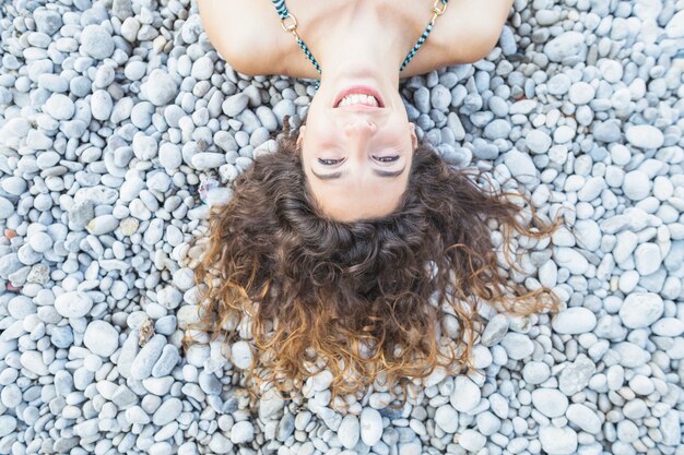 An overhead view of smiling young woman laying on pebbles