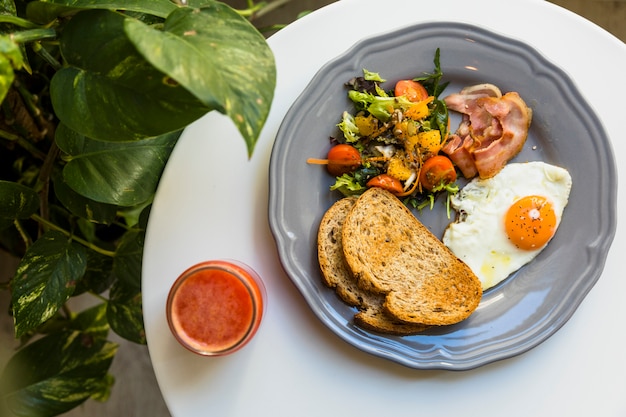 An overhead view of smoothie and breakfast on ceramic plate over the white table near the epipremnum aureum plant