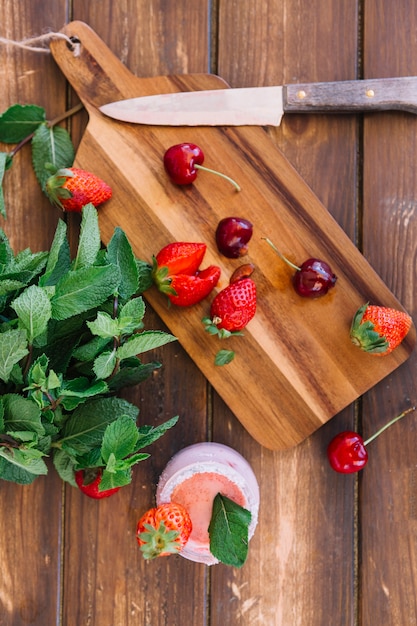 Overhead view of smoothie; mint leaf near cherries and strawberries on cutting board