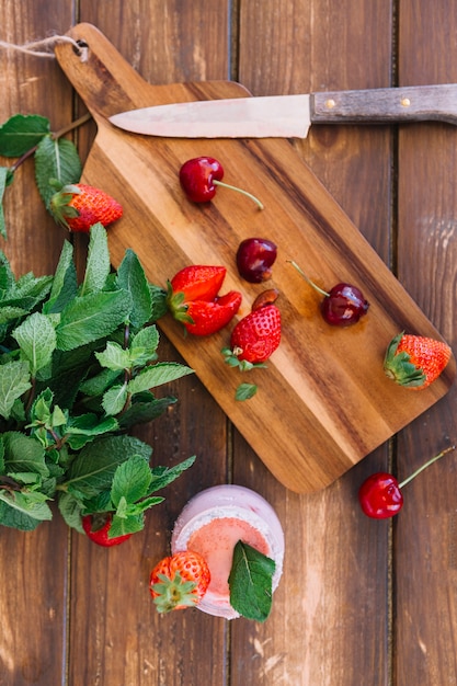 스무디의 오버 헤드보기; 체리와 커팅 보드에 딸기 근처 민트 잎