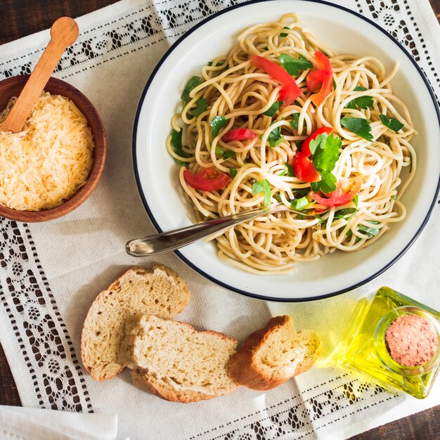 Верхний вид спагетти на тарелке с тертым сыром; хлеб и оливковое масло на коврике