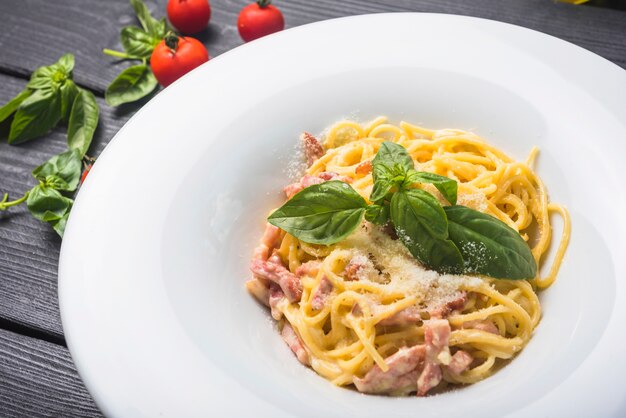 An overhead view of spaghetti with basil leaf and cheese toppings on white plate