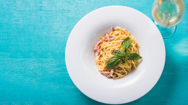 An overhead view of spaghetti with wineglass on turquoise background