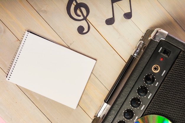 An overhead view of spiral notepad; musical note and amplifier on wooden desk