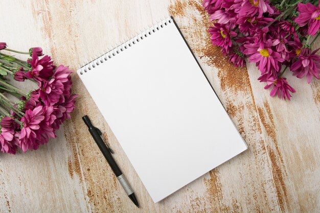 Overhead view of spiral notepad with pen and pink flowers on wooden background