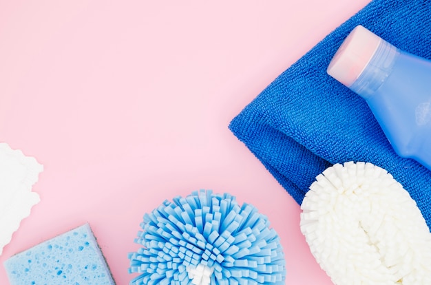 An overhead view of sponge; detergent bottle; napkin against pink backdrop