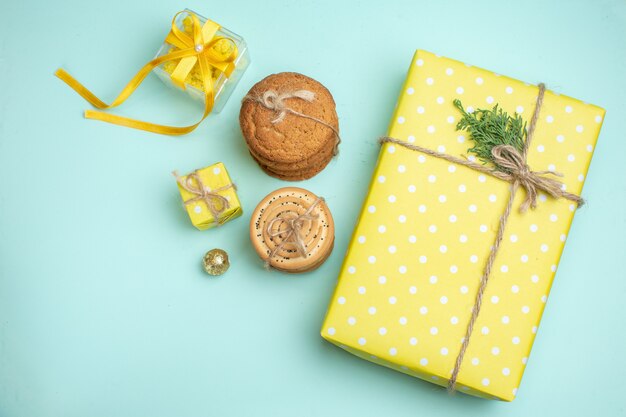 파스텔 녹색 배경의 장식 액세서리 옆에 쌓인 다양한 맛있는 쿠키와 아름다운 노란색 선물 상자의 머리 위