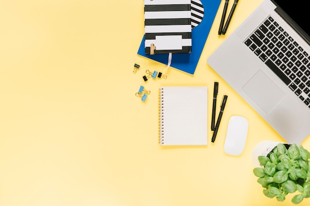 Overhead view of stationery with laptop and mouse on paper yellow background