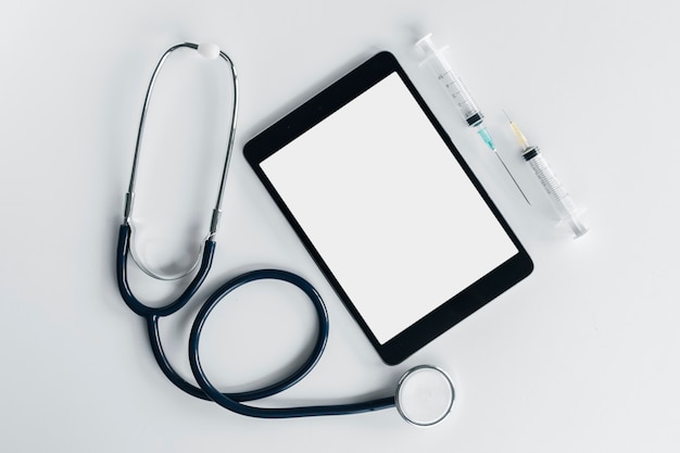 An overhead view of stethoscope; digital tablet and syringe isolated on white background