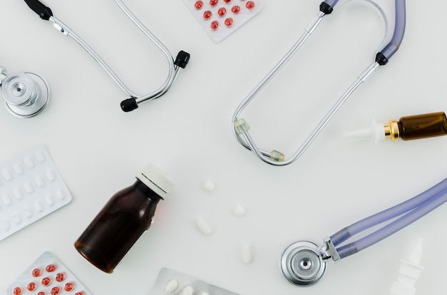 Вид сверху стетоскопа; таблетки; бутылка и назальный спрей на белом фоне