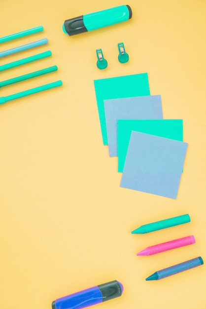 Overhead view of sticky note; highlighter and crayons on yellow background