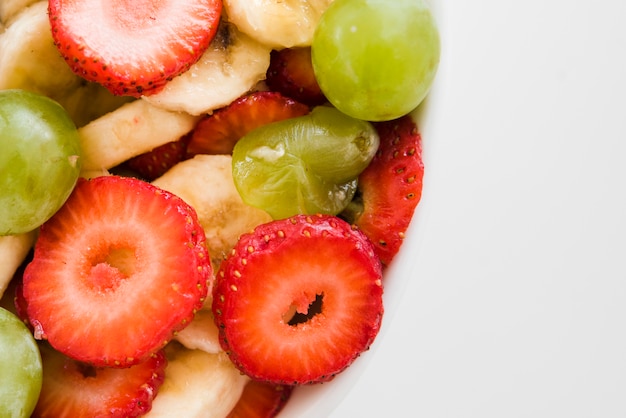 An overhead view of strawberry and banana slices with grapes on white background