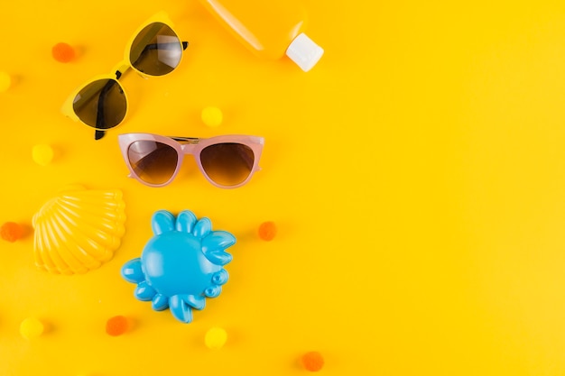 Вид сверху на солнцезащитные очки; бутылка солнцезащитного крема; игрушка гребешок и краб на желтом фоне