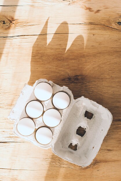 Вид сверху солнечного света, падающего на коробку белых яиц на деревянном фоне