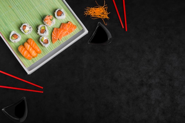 An overhead view of sushi roll with grated carrot and red chopsticks against black backdrop