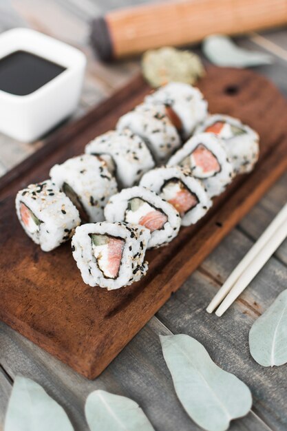 An overhead view of sushi roll on wooden tray with soya sauce and chopstick on wooden table
