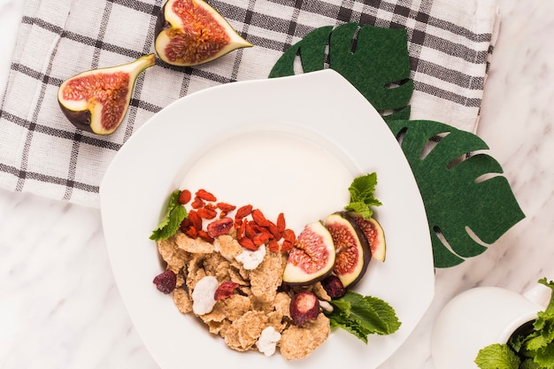 Overhead view of tasty breakfast; fake monstera leaves and kitchen cloth over white marble backdrop