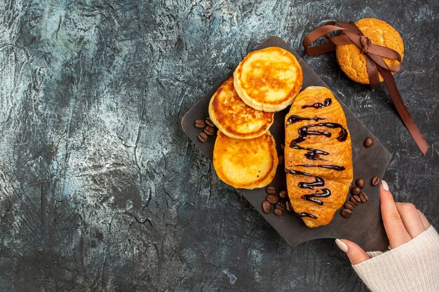 Overhead view of tasty breakfast with pancakes croisasant stacked cookies on dark background