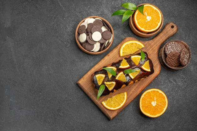 Overhead view of tasty cakes cut oranges with biscuits on cutting board on black table