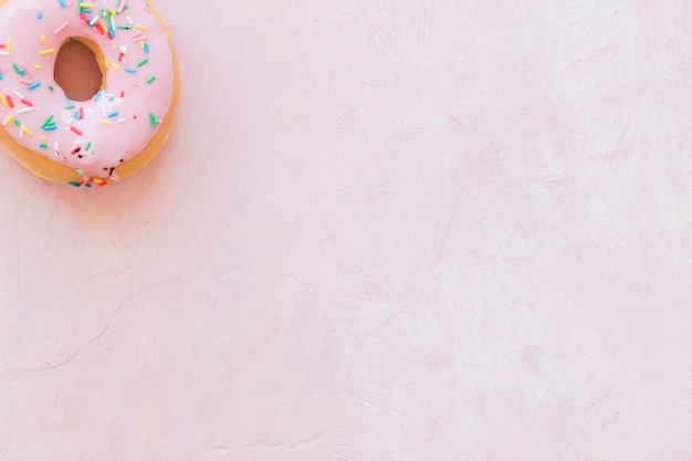 Верхний вид вкусного пончика с брызгами на розовом фоне