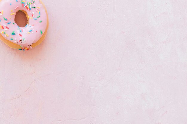 Overhead view of tasty donut with sprinkles on pink backdrop