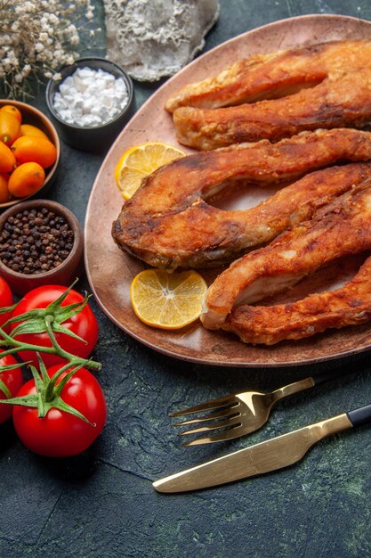 Overhead view of tasty fried fishes and lemon slices on a brown plate tomatoes kumquats on mix colors table with free space