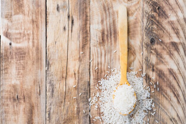 Overhead view of tasty raw rice spilling out of wooden spoon with space for text