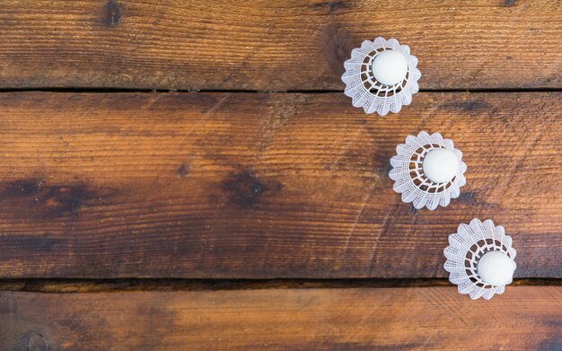 An overhead view of three white shuttlecocks on wooden plank background