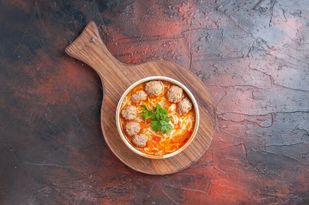 Overhead view of tomato meatballs soup with noodles in a brown bowl on dark background