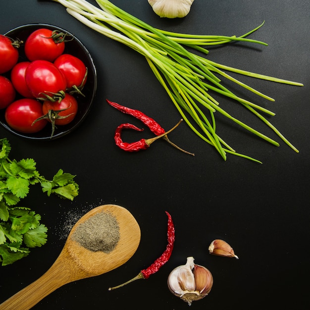 Overhead view of tomato; red chilies; spring onion; garlic; parsley and spices over black background