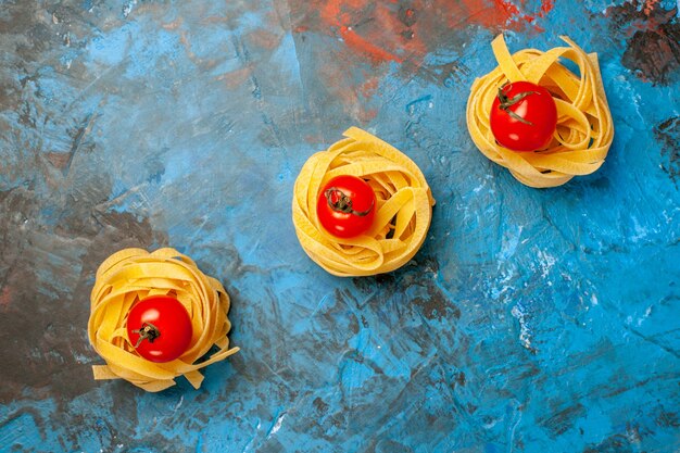 Overhead view of tomatoes on homemade pastas lined up in a row on blue background