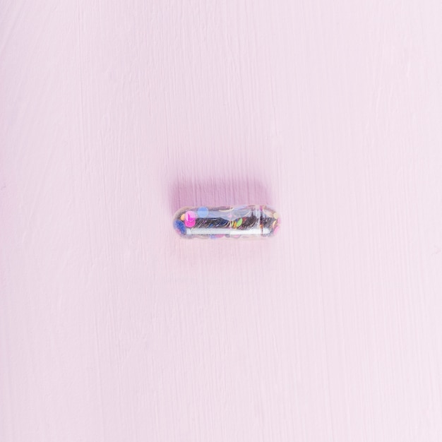Overhead view of transparent sequin capsule on pink backdrop