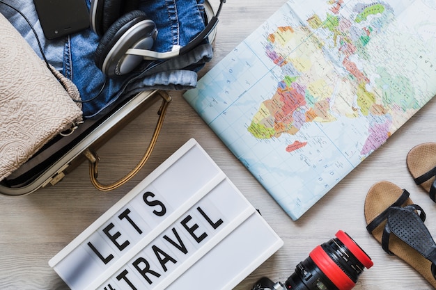 Overhead view of travelling bag, map, camera, and pair of footwear on wooden table