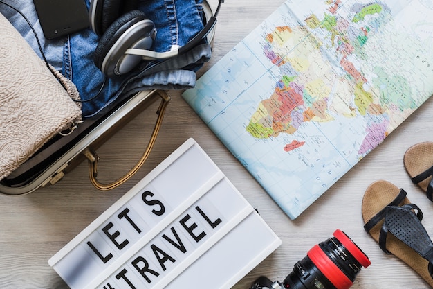 旅行用バッグ、地図、カメラ、および靴のペアの木製テーブル上のオーバーヘッドビュー
