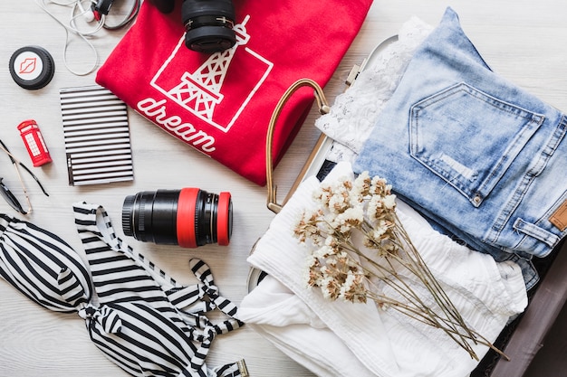 Overhead view of travelling bag with female outfits and flowers