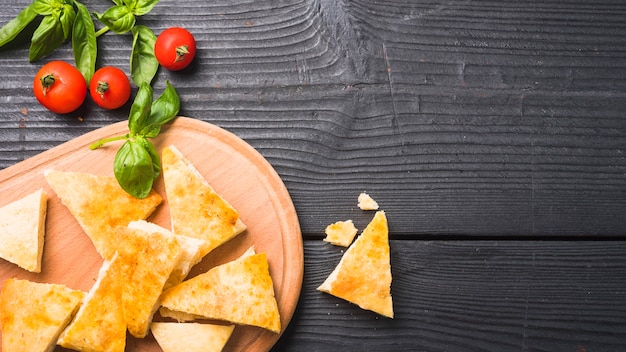 An overhead view of triangular bread pieces with basil leaves and tomatoes