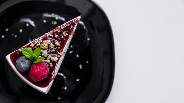 An overhead view of triangular cheesecake with raspberry; blueberry and mints on black ceramic plate against white background