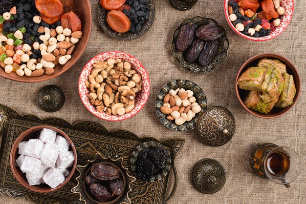 An overhead view of turkish tea; dates; lukum; dried fruits and nuts on jute tablecloth