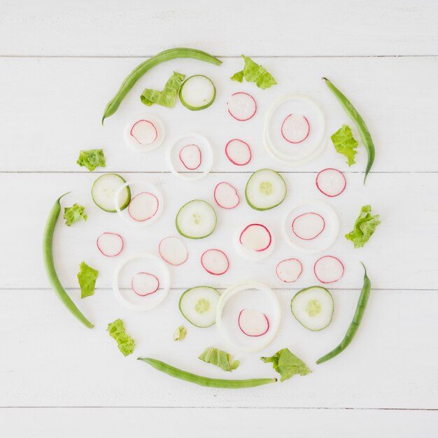 An overhead view of turnip; onion and cucumber slices with green french beans and lettuce on wooden desk