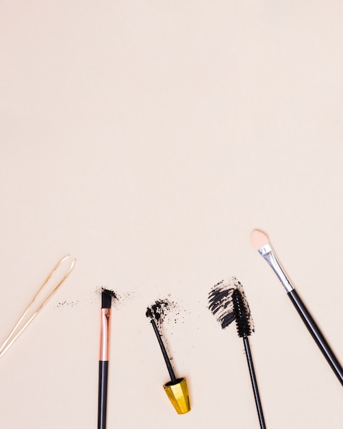 An overhead view of tweezers; makeup brush and mascara brush isolated on beige background