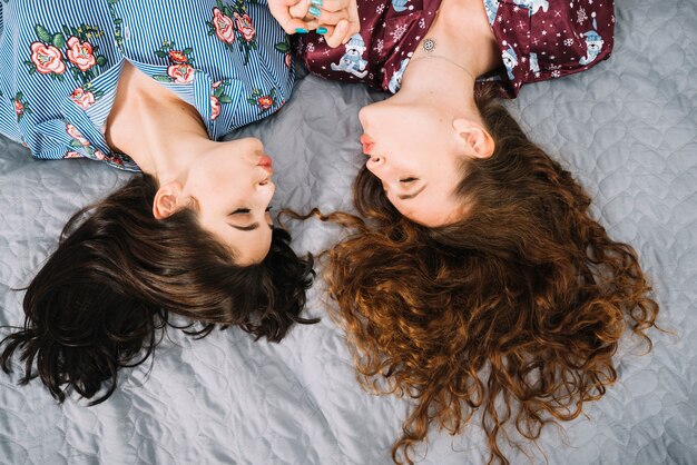 Overhead view of two female friends pouting lips while lying on bed